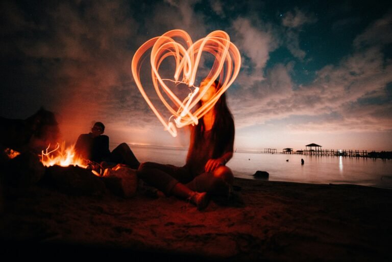 chica en la playa atardecer corazón con laser naranja fuego al fondo